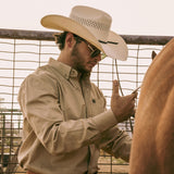 Bearded man wearing a 10X Cowboy Weston black and ivory cowboy hat with a white collared shirt putting saddle on a brown horse