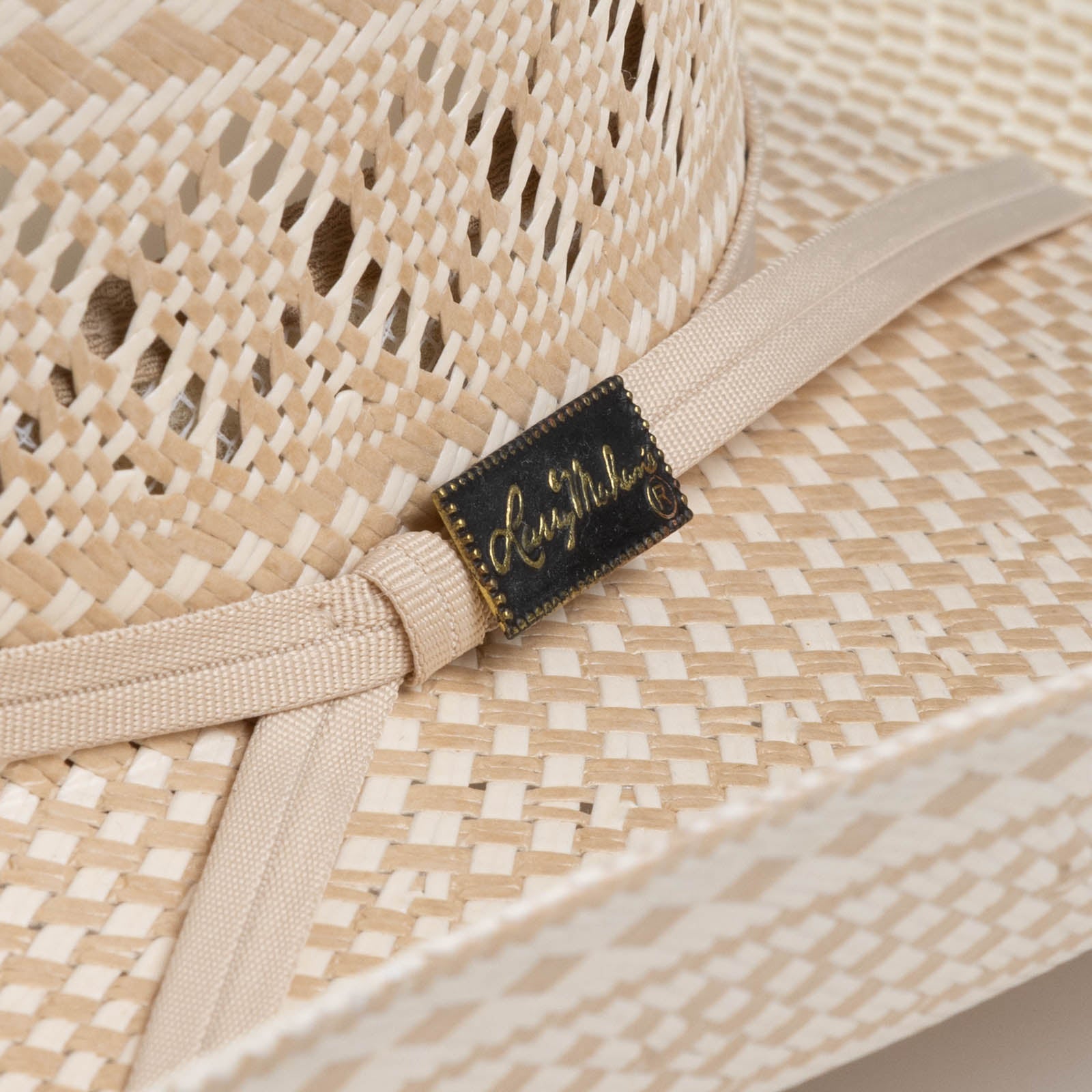 10X Cowboy Cruz tan and ivory cowboy hat closeup of buckle as a black rectangle with golden dots around the outside and Larry Mahan's logo on the inside