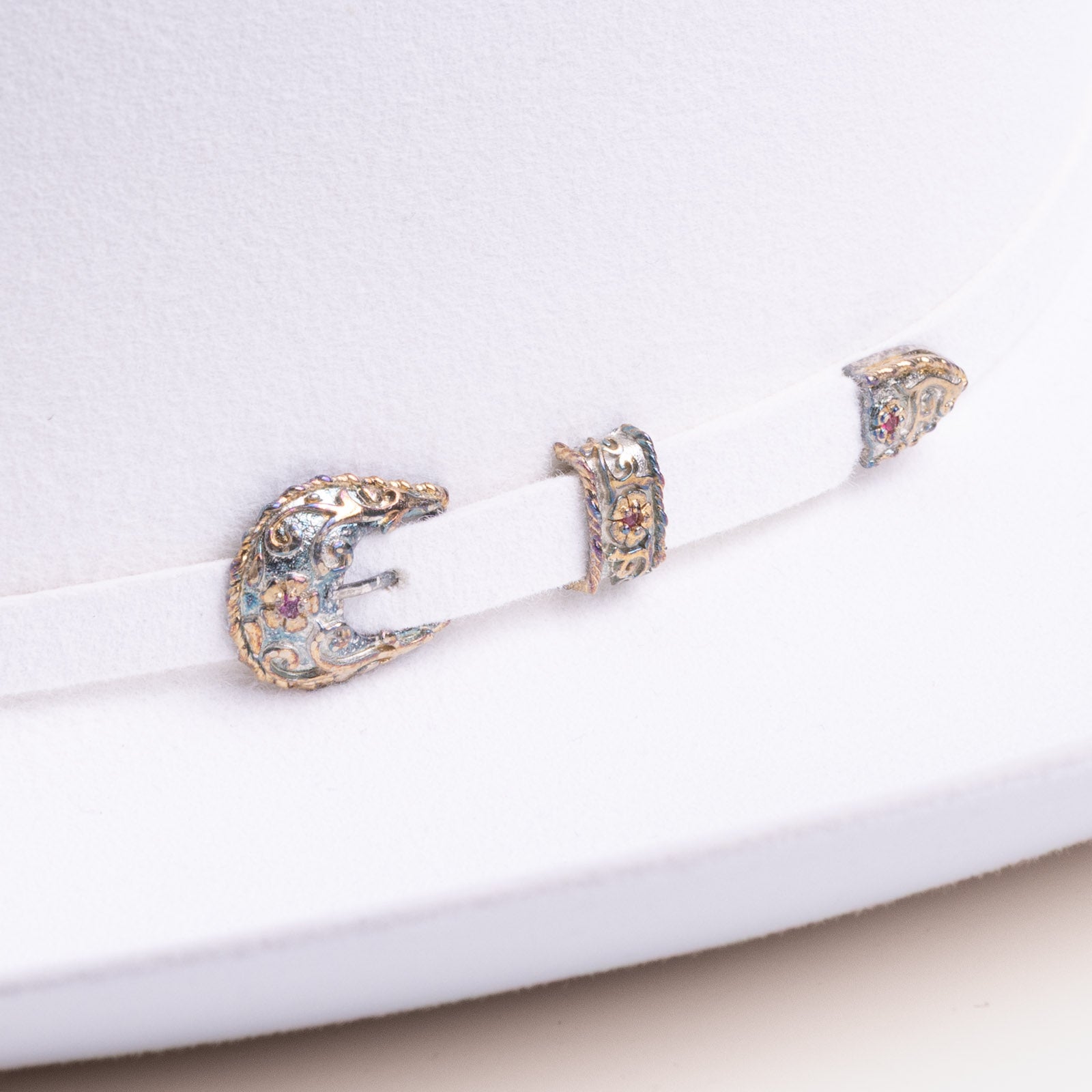 30X El Rey white cowboy hat closeup of buckle as a gold and blue buckle with a few red gems inlaid in the middle on a white band