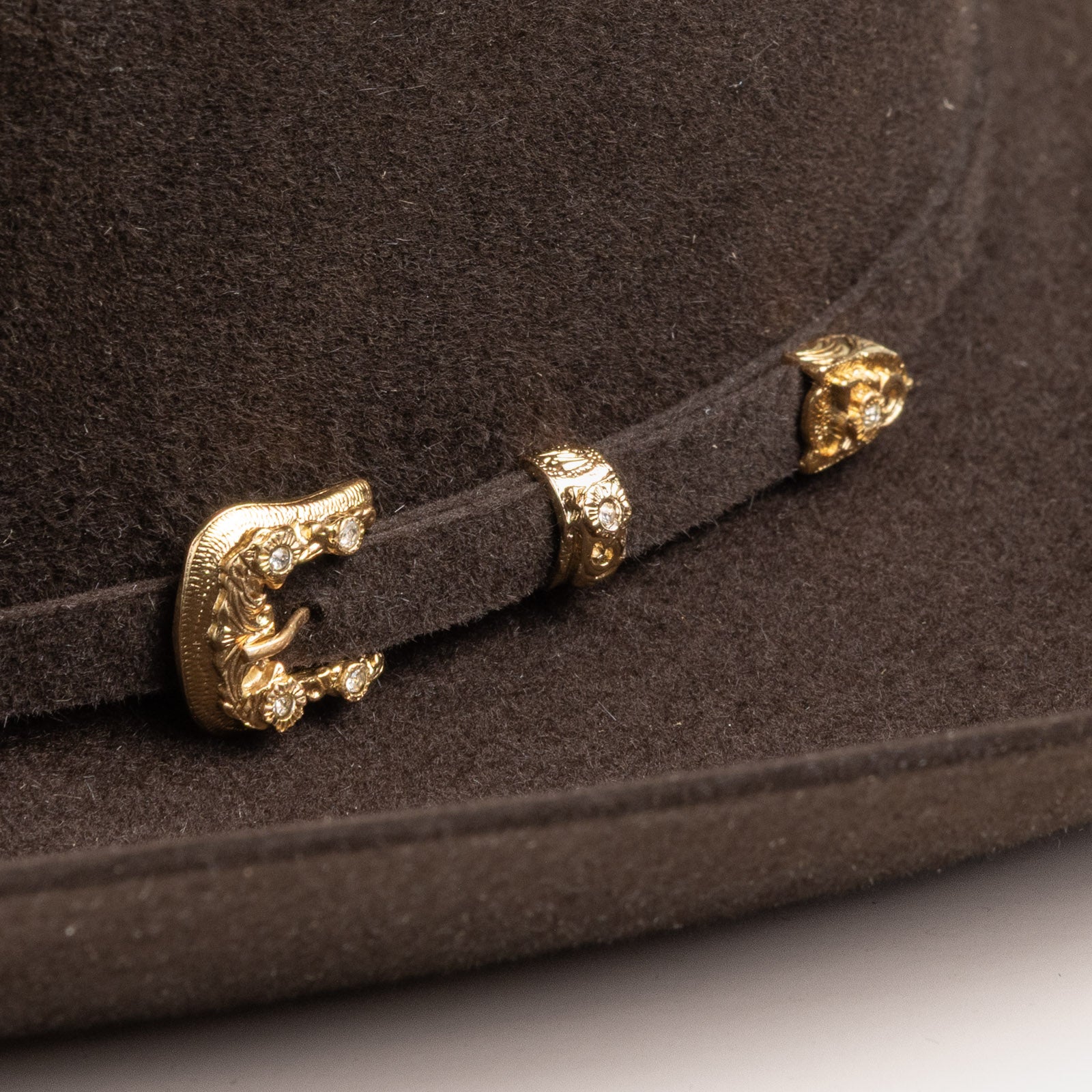 30X Opulento brown cowboy hat closeup of buckle in gold with small silver gems inlaid on the edges on a brown band