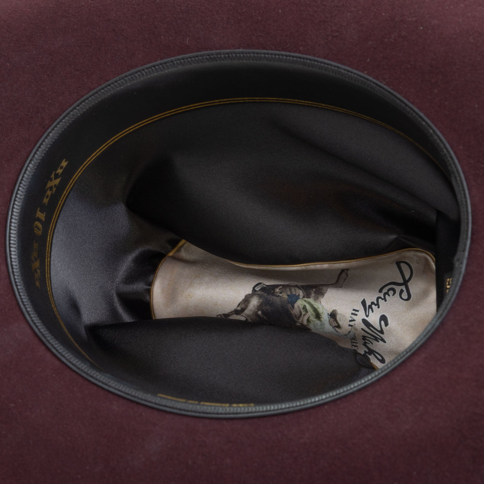 10X Jerarca black cherry cowboy hat closeup of the underside with black interior, gold trim and lettering