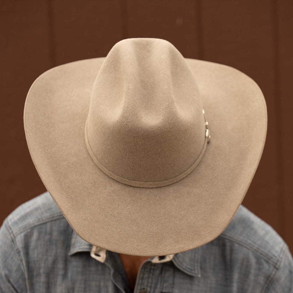 Bearded man wearing a 5X Fort Worth natural cowboy hat and blue long sleeve shirt looking downward to display the top of his hat