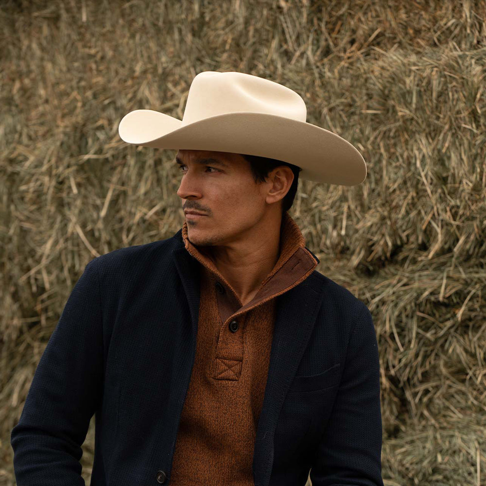 Man wearing a 10X Jerarca belly cowboy hat, blue jacket with brown sweater underneath with a high collar looking to the left