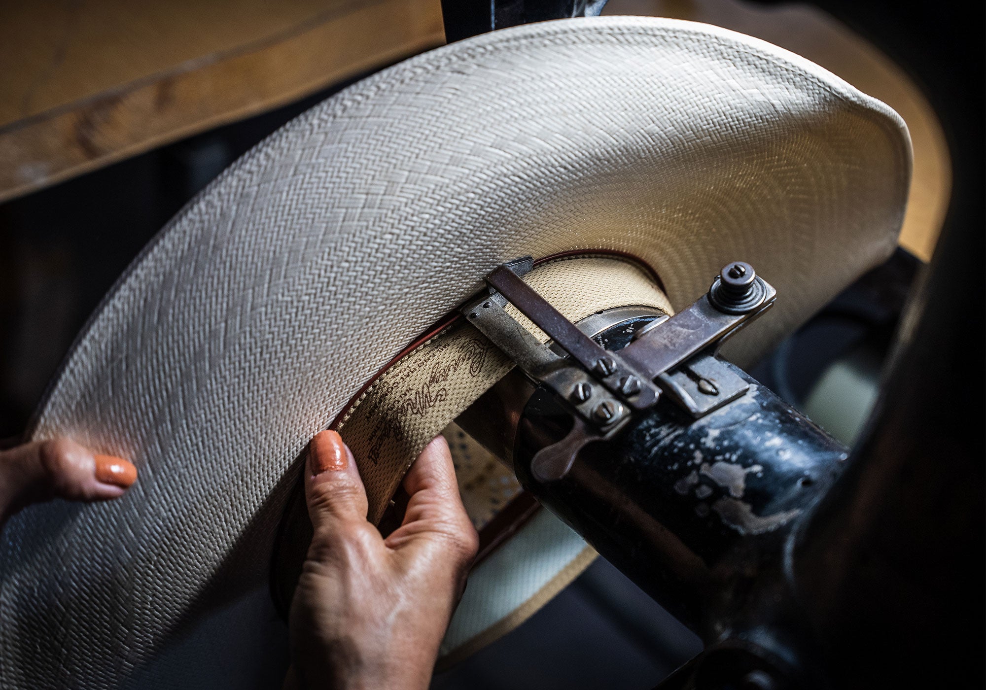 Woman's hands holding a white hat to use a machine to stitch a tan band to the underside of it