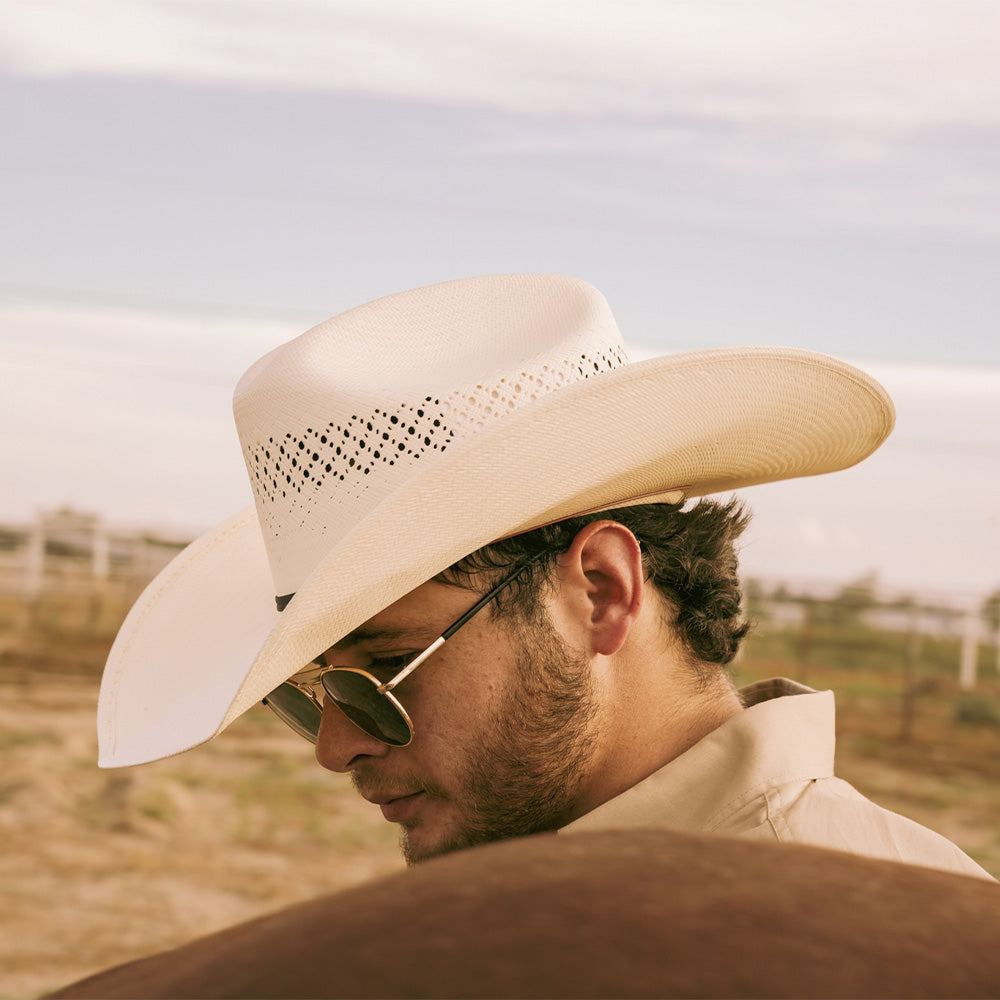 Bearded man wearing a 10X Cowboy Weston black and ivory cowboy hat with a white collared shirt standing behind a brown horse