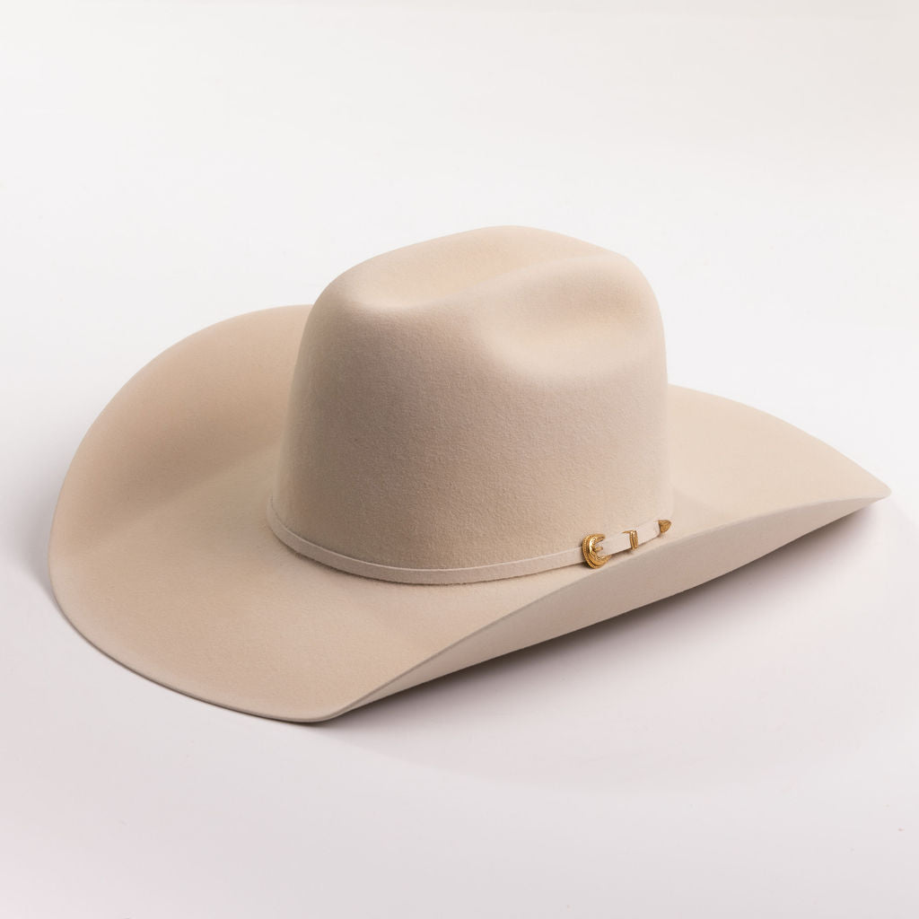 A light beige felt cowboy hat with a small gold buckle detail on the side, photographed on a clean light gray background