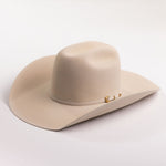 A light beige felt cowboy hat with a small gold buckle detail on the side, photographed on a clean light gray background