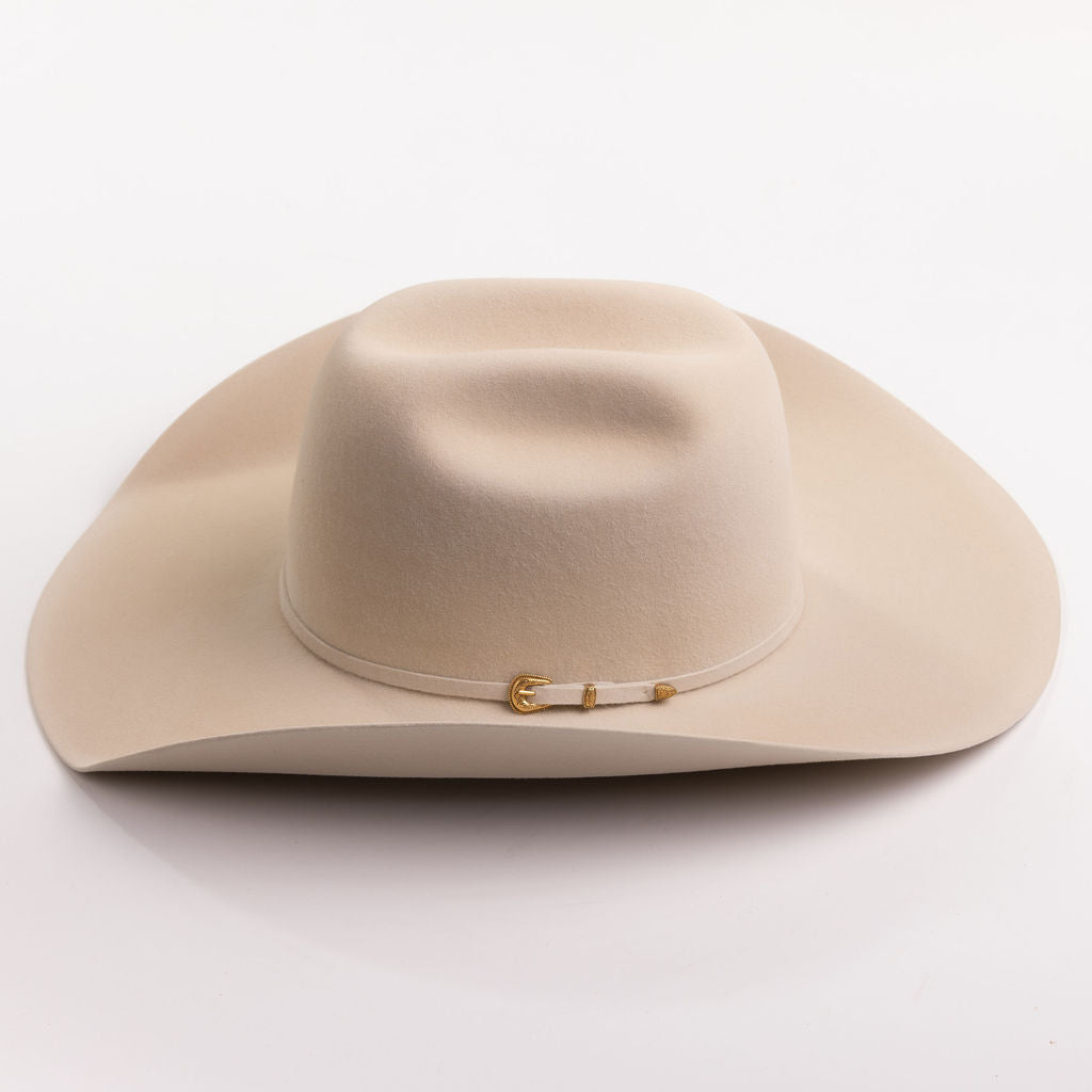 A light beige felt cowboy hat with a small gold buckle detail on the side, photographed on a clean light gray background