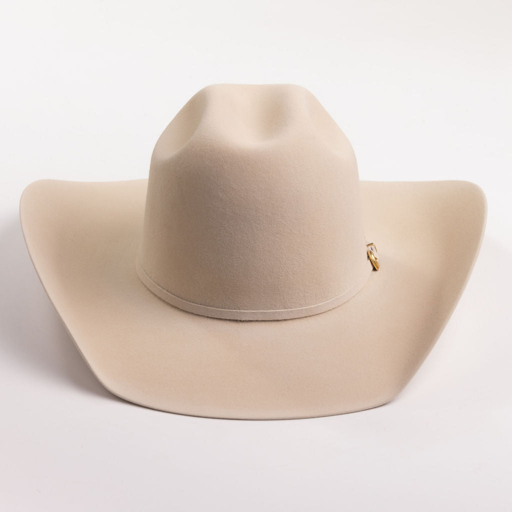 A light beige felt cowboy hat with a small gold buckle detail on the side, photographed on a clean light gray background