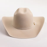 A light beige felt cowboy hat with a small gold buckle detail on the side, photographed on a clean light gray background