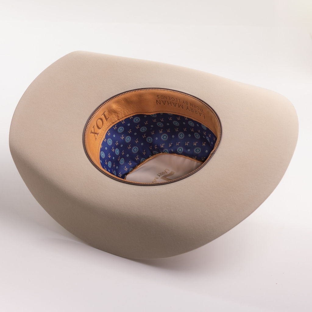 A light beige cowboy hat shown from a three-quarters angle, displaying its patterned blue and orange patterned inner crown lining