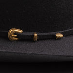 Close-up of a black felt hat with an engraved gold buckle and matching gold decorative accents on the hatband