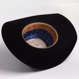 A black cowboy hat shown from an overhead angle, displaying its tan leather-look interior band and a blue patterned inner lining with gold details