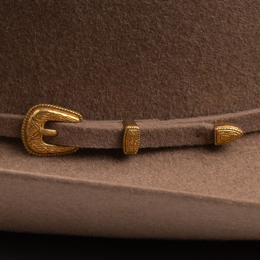 Close-up of a fawn brown felt hat with a matching brown strap and ornate gold-tone buckle and decorative accents