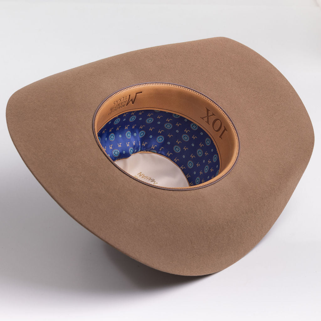 A fawn brown colored cowboy hat shown from an angled top-down view on a light gray background, displaying its patterned blue interior lining and tan leather-like inner band with 10X branding.