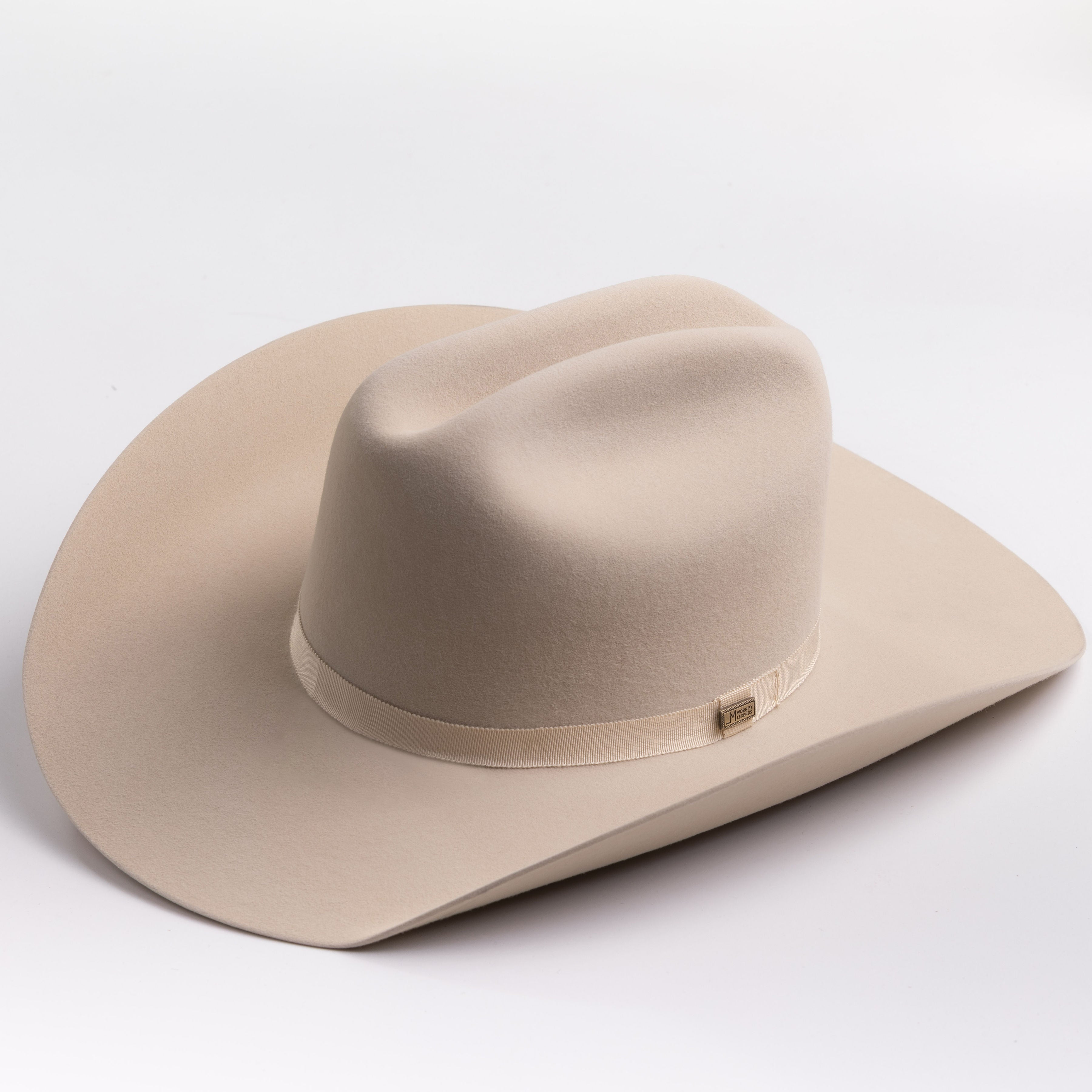 A light beige felt cowboy hat with a matching band and a small gold-toned buckle, photographed on a clean light gray background