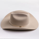 A light beige felt cowboy hat with a matching band and a small gold-toned buckle, photographed on a clean light gray background