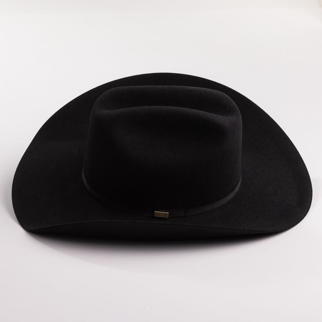 A black felt cowboy hat with a curved brim and a small gold brand plaque on the band, photographed on a light gray background