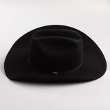A black felt cowboy hat with a curved brim and a small gold brand plaque on the band, photographed on a light gray background