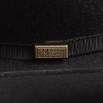 Close-up of a black felt hat with a black ribbon band and a rectangular gold-tone metal pin engraved with the brand "Worn by Legends"