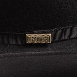 Close-up of a black felt hat with a black ribbon band and a rectangular gold-tone metal pin engraved with the brand "Worn by Legends"