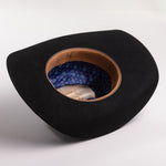 A black wide-brimmed cowboy hat shown from an overhead angle, displaying its tan leather interior band and blue patterned inner lining