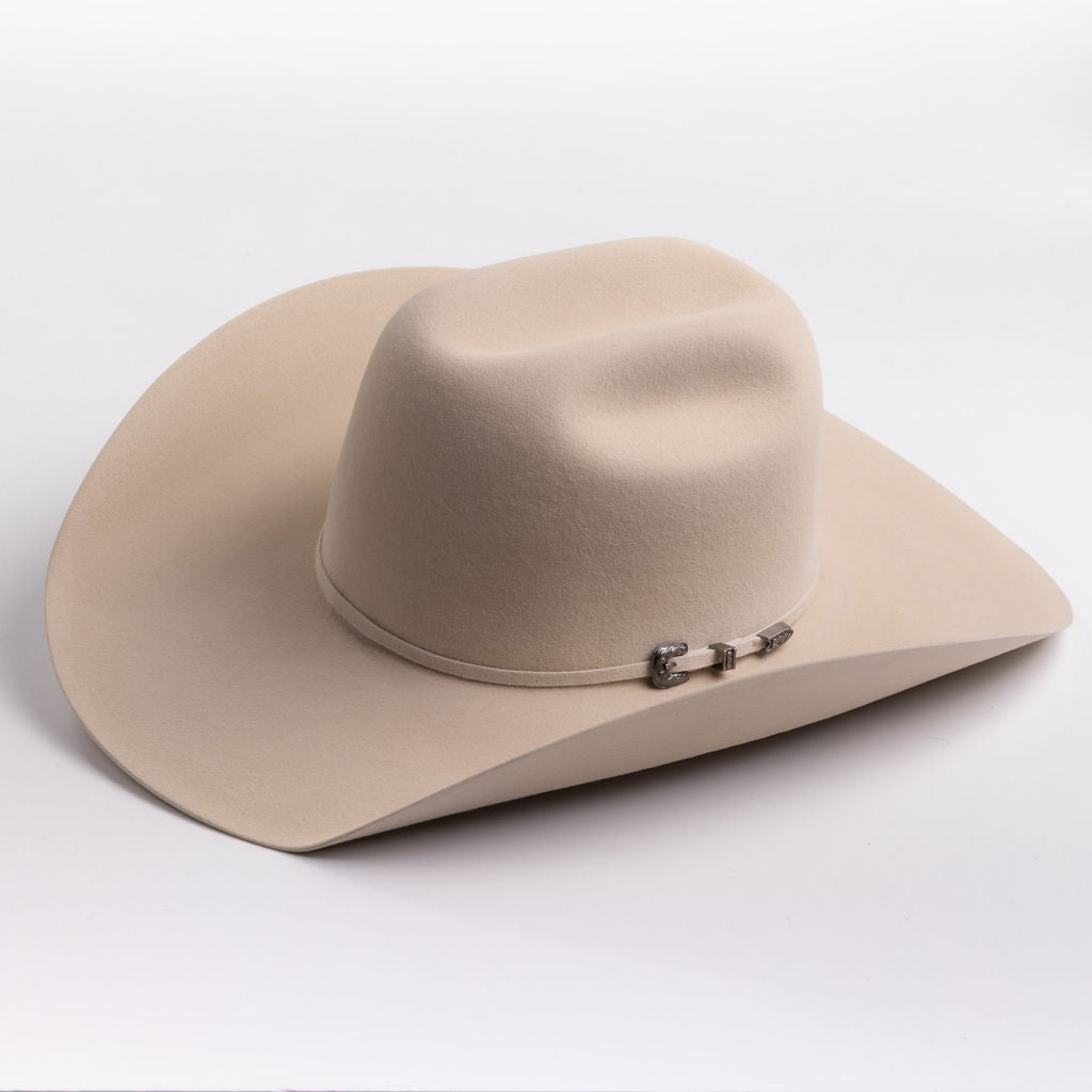A light beige felt cowboy hat with a curved brim and a small silver buckle detail on the band, photographed on a clean light gray background