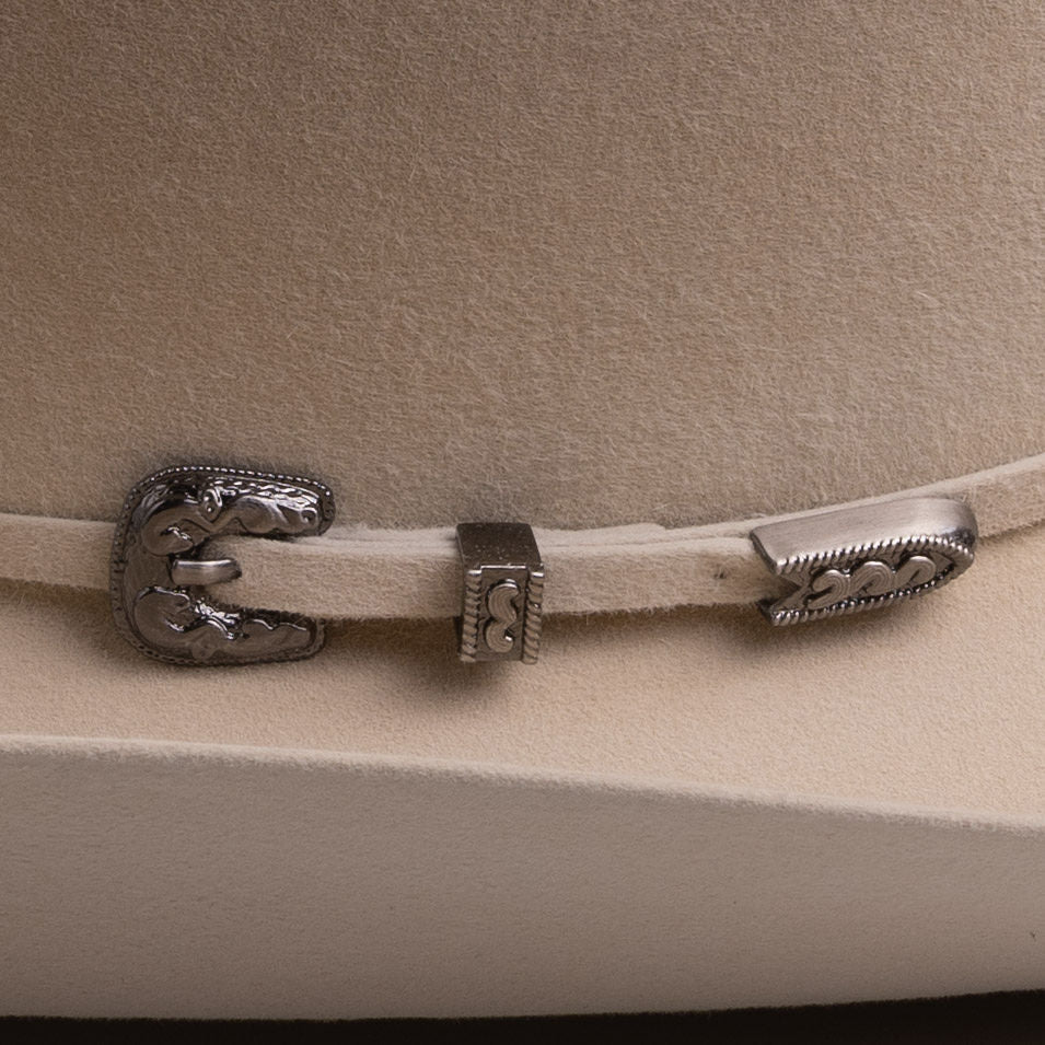 Close-up of a light beige felt cowboy hat featuring a decorative silver-toned metal buckle and strap closure