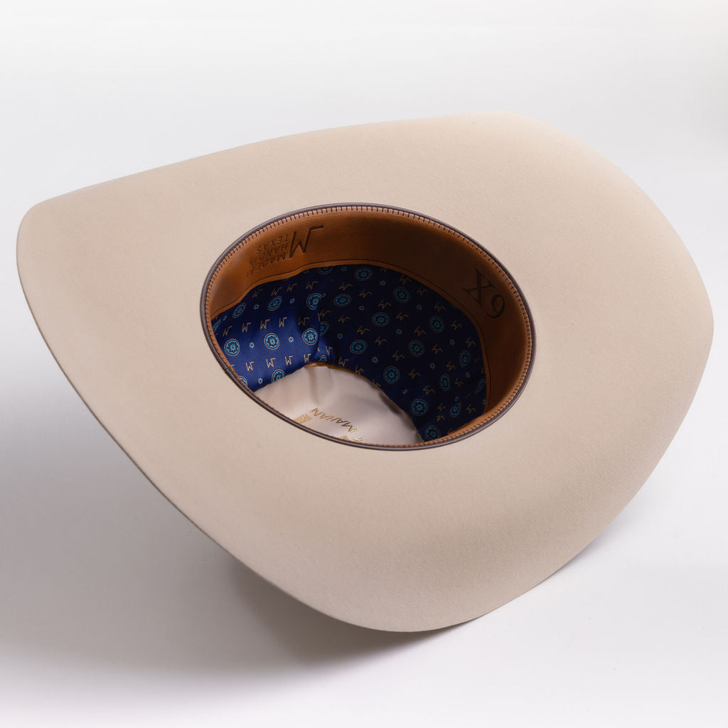A light beige wide-brim cowboy hat shown from an overhead angle, displaying its brown leather interior band and blue patterned inner lining