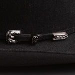 A close-up of a black felt hat featuring a decorative silver-toned metal buckle closure with a sculpted animal head design