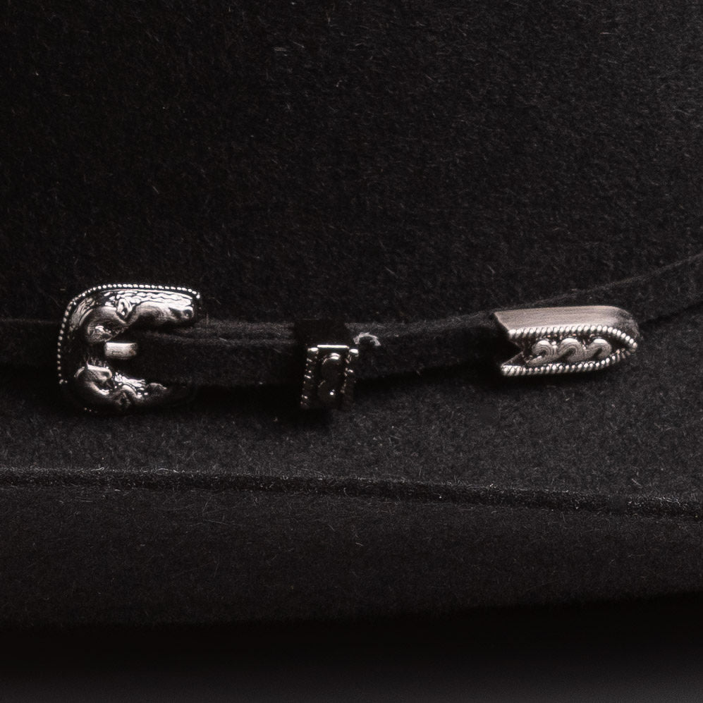A close-up of a black felt hat featuring a decorative silver-toned metal buckle closure with a sculpted animal head design