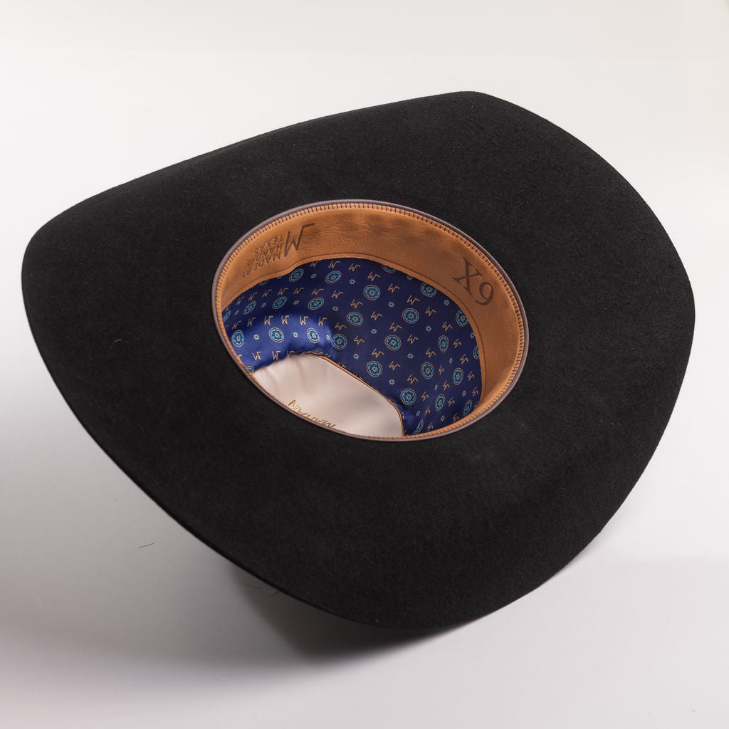A black felt cowboy hat shown from an overhead angle, displaying its brown leather inner band and a blue patterned interior lining