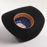 A black felt cowboy hat shown from an overhead angle, displaying its brown leather inner band and a blue patterned interior lining