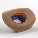 A tan cowboy hat with a wide brim, shown from a three-quarters perspective to reveal the interior; the hat features a patterned blue inner band with small white stars and a tan leather trim