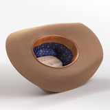 A tan cowboy hat with a wide brim, shown from a three-quarters perspective to reveal the interior; the hat features a patterned blue inner band with small white stars and a tan leather trim