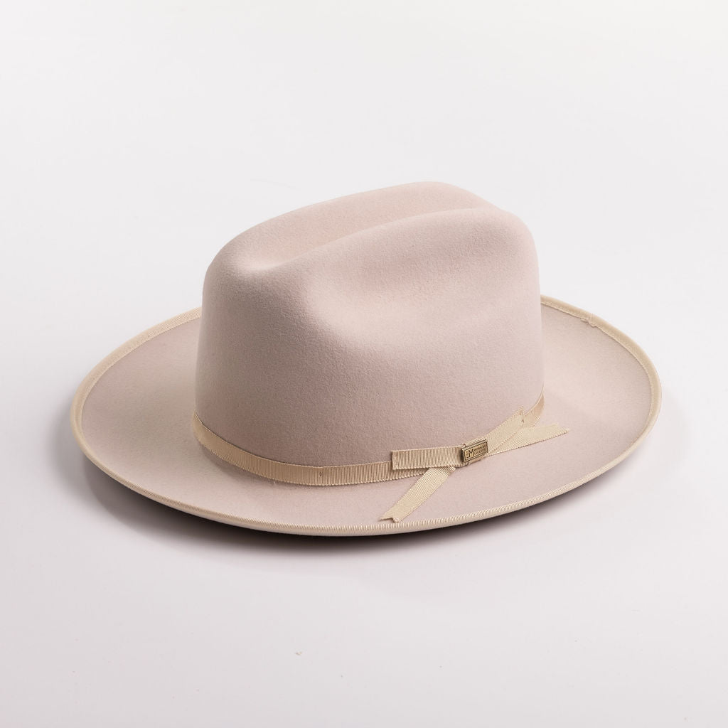 A light beige belly colored felt hat with a matching beige ribbon band and small gold-tone buckle, photographed on a light gray background