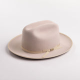A light beige belly colored felt hat with a matching beige ribbon band and small gold-tone buckle, photographed on a light gray background