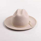 A light beige belly colored felt hat with a matching beige ribbon band and small gold-tone buckle, photographed on a light gray background