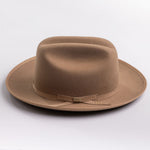 A classic felt hat in a fawn brown color, featuring a matching fabric band with a small decorative buckle, photographed on a light gray background