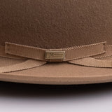 Close-up of a brown felt hat with a matching grosgrain ribbon bow and a small metal brand plaque reading "LM WORN BY LEGENDS"