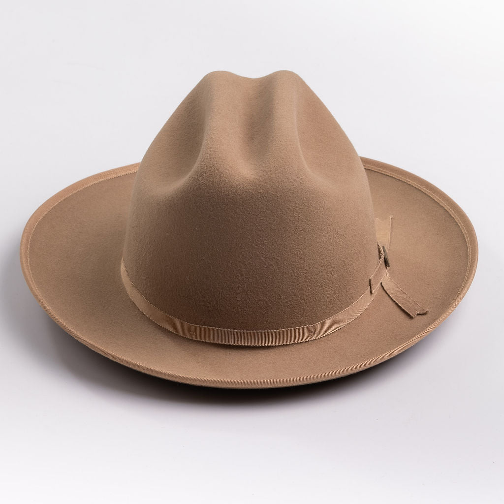 A classic felt hat in a fawn brown color, featuring a matching fabric band with a small decorative buckle, photographed on a light gray background
