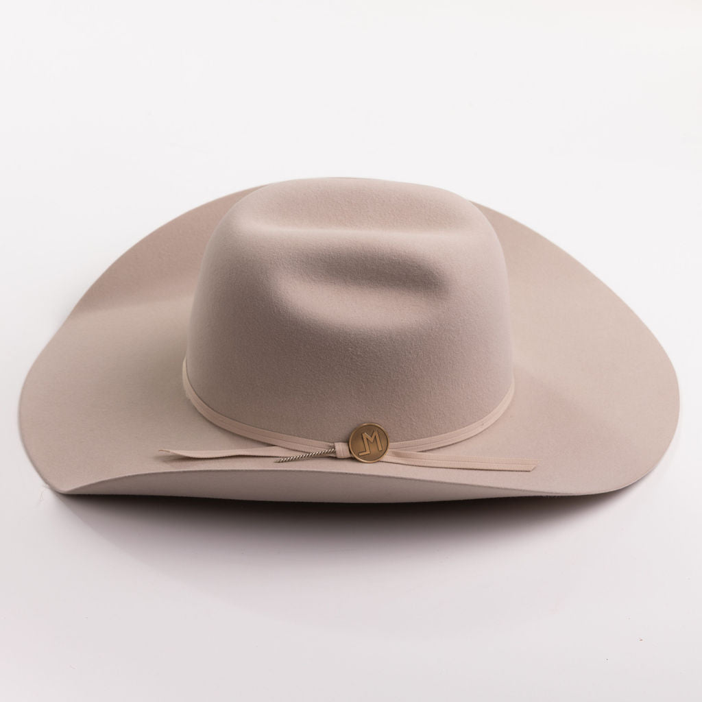 A light beige felt cowboy hat with a matching band and a small round gold-tone button, photographed on a clean light gray background