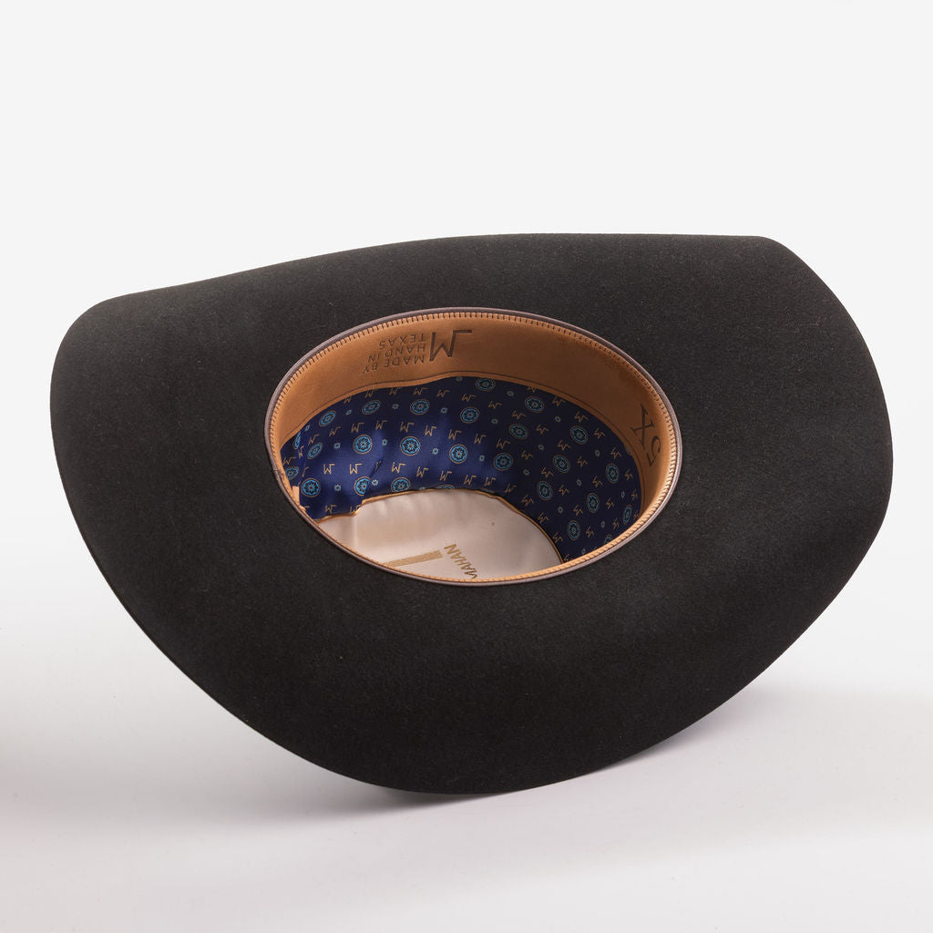 A black felt cowboy hat shown from an angled top-down view, displaying its tan leather trim and a blue patterned inner lining with gold lettering