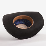 A black felt cowboy hat shown from an angled top-down view, displaying its tan leather trim and a blue patterned inner lining with gold lettering