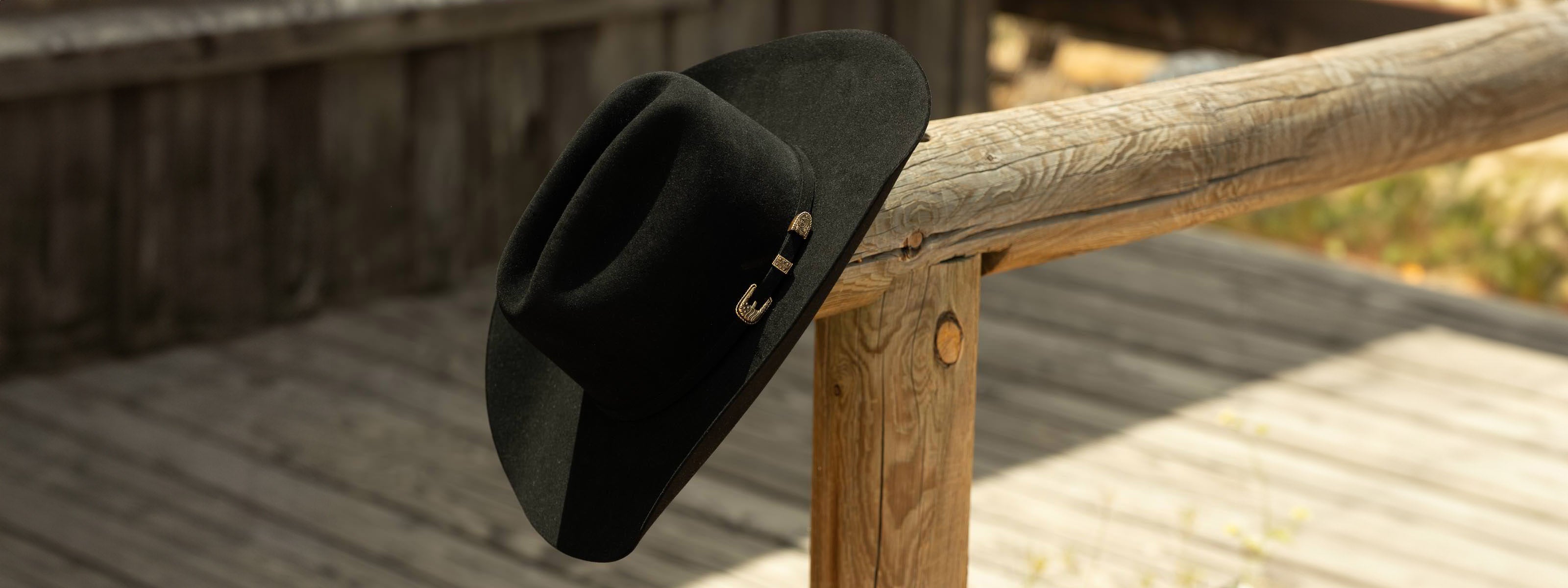 Black felt cowboy hat on a wooden railing with a rustic background
