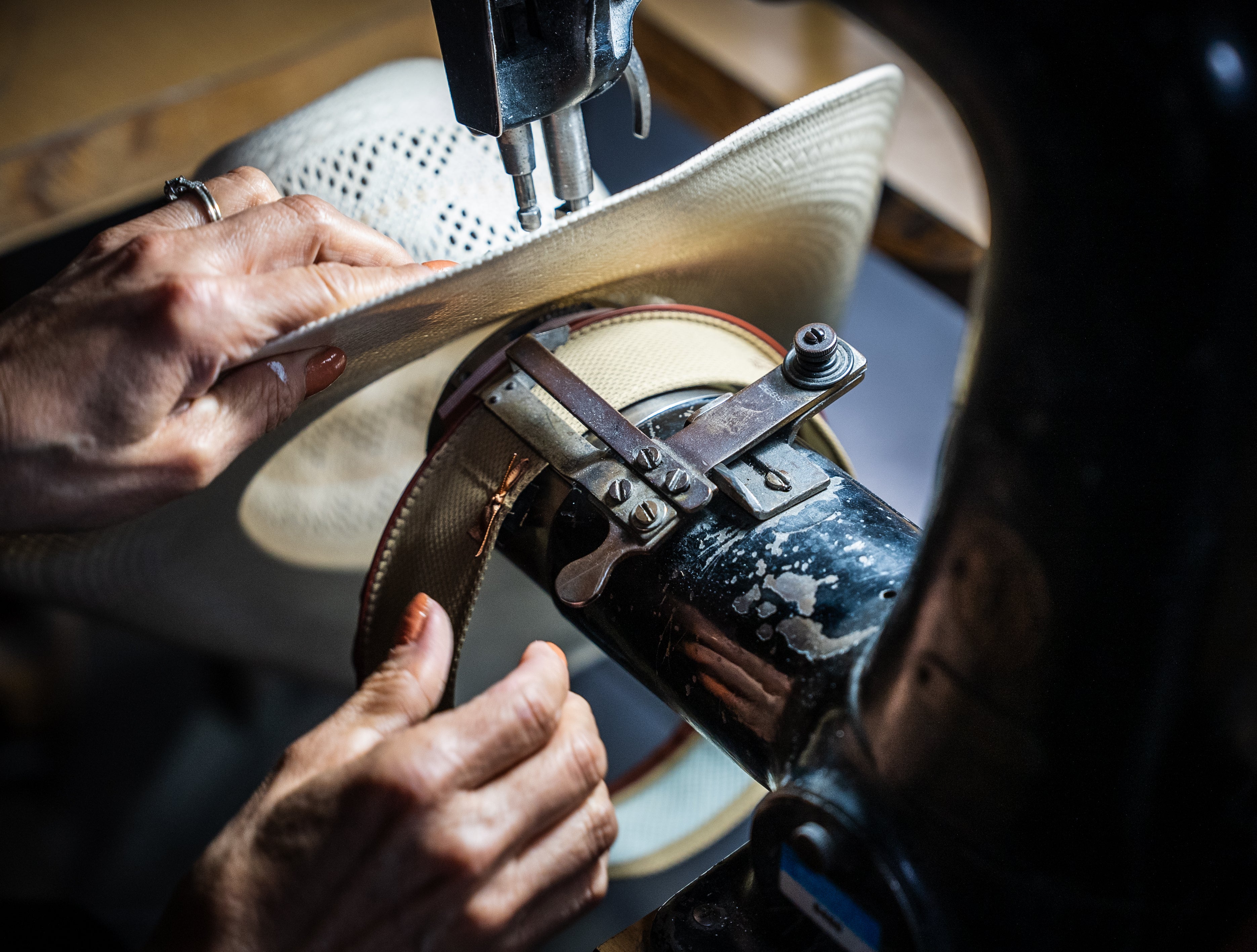 Person working on a straw hat with a sewing machine.