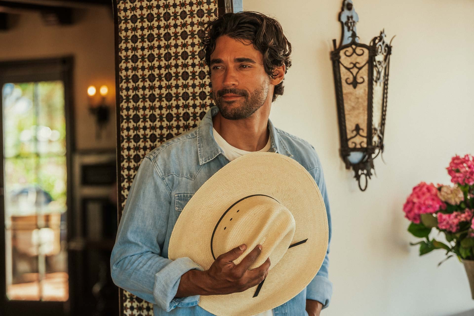 Man holding a cowboy hat in a room with decorative elements and flowers.
