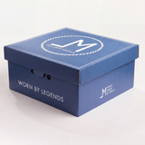 A blue branded product box laid down face up with a white circular logo and the text "WORN BY LEGENDS" and "HAND MADE IN TEXAS" on a clean white background