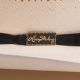 Close-up of a woven straw hat with a black ribbon band and a gold-embossed patch reading "Larry Mahan's"