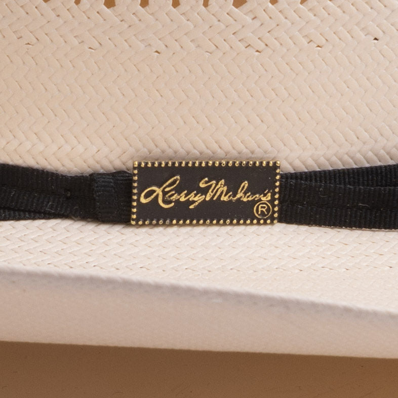 Close-up of a woven straw hat with a black ribbon band and a gold-embossed patch reading "Larry Mahan's"